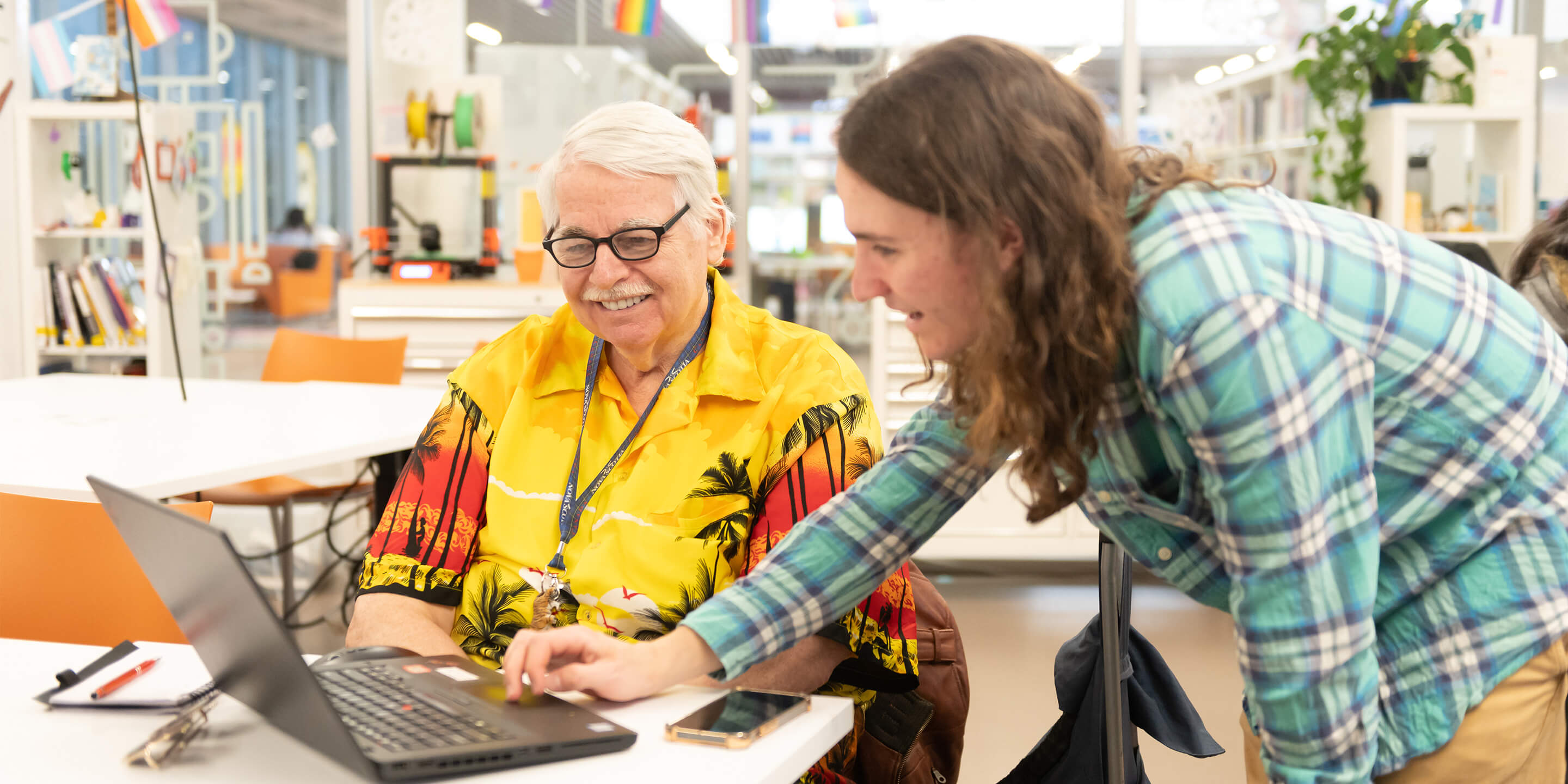 2 people and a laptop at the Library, one person is demonstrating or guiding the other.